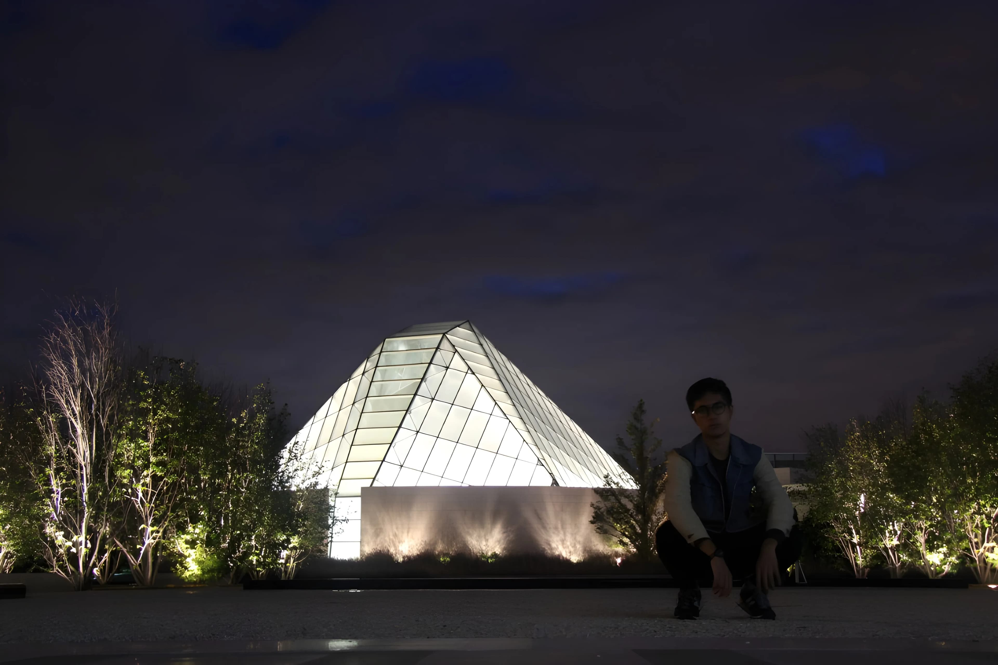 Matthew at night in front of a lit glass pyramid